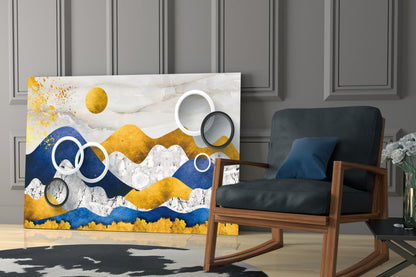 Abstract mountain landscape glass wall art with blue, gold, and white layered peaks and circular metallic elements displayed in modern living room setting.