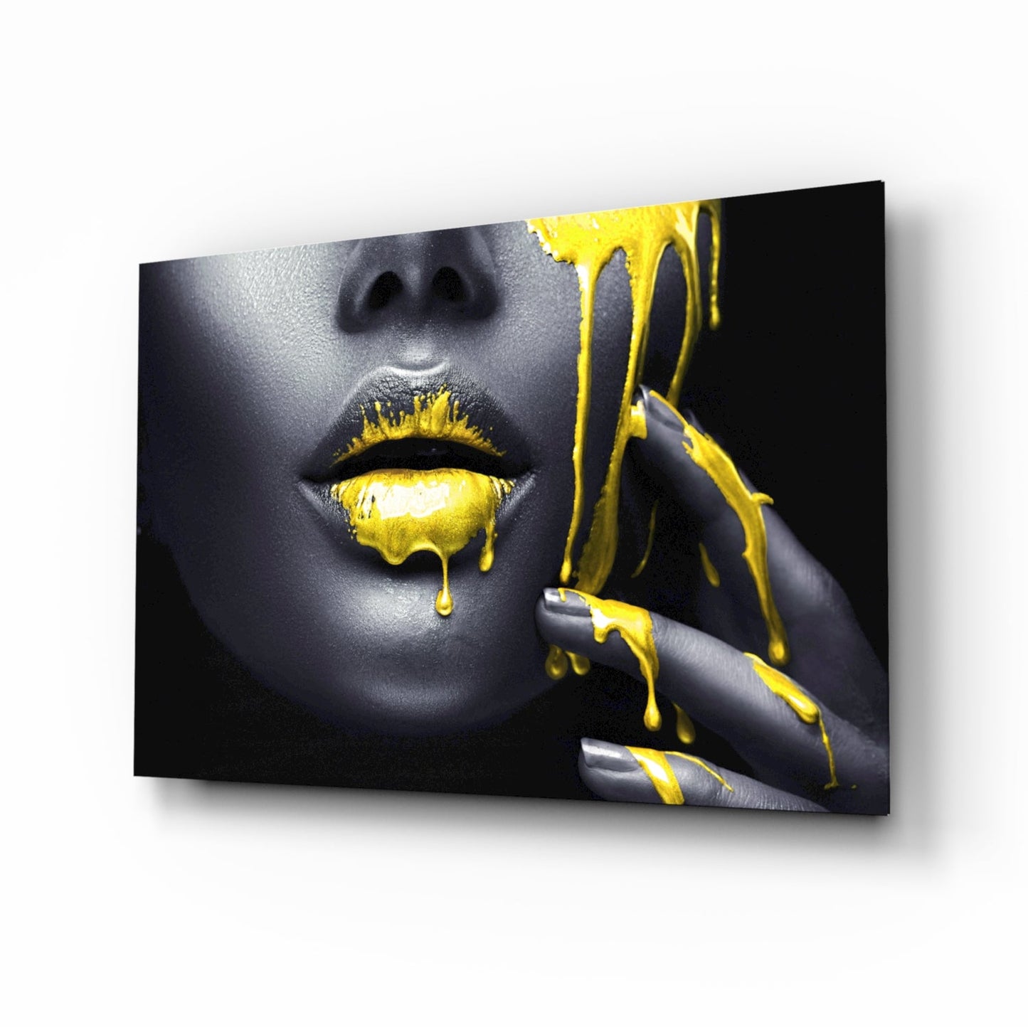 Glass wall art displaying a woman's face with gray skin and bright yellow paint dripping from lips and fingers against black background.