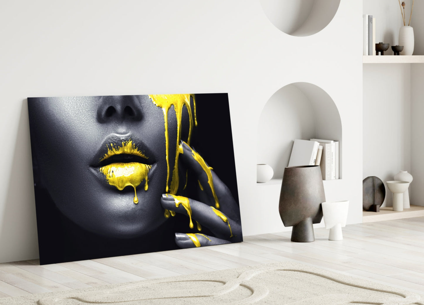 Black and gold glass wall art featuring a woman's face with yellow paint dripping from lips, leaning against white interior wall.