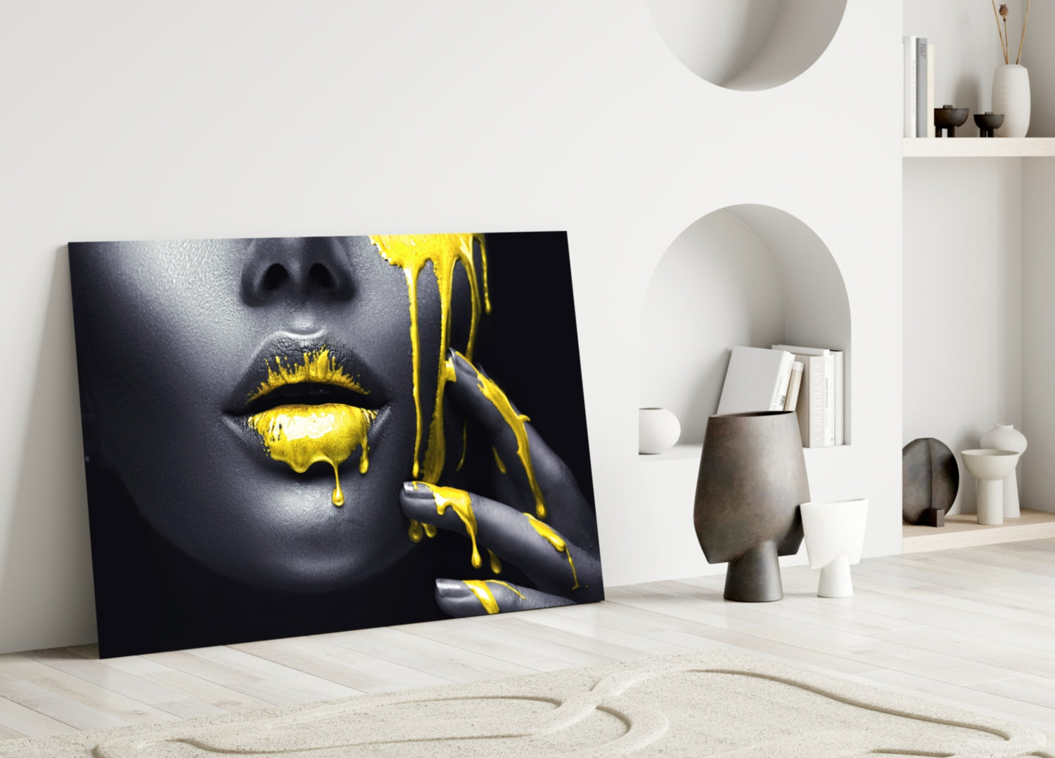 Black and gold glass wall art featuring a woman's face with yellow paint dripping from lips, leaning against white interior wall.
