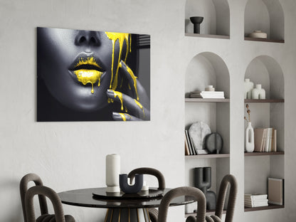 Glass wall art displaying a woman's face with gold dripping paint effect, hung above a black dining table in a modern interior.