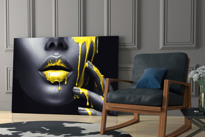 Glass wall art displaying a woman's face with gray skin and bright yellow dripping paint effect, displayed in a modern living room setting.