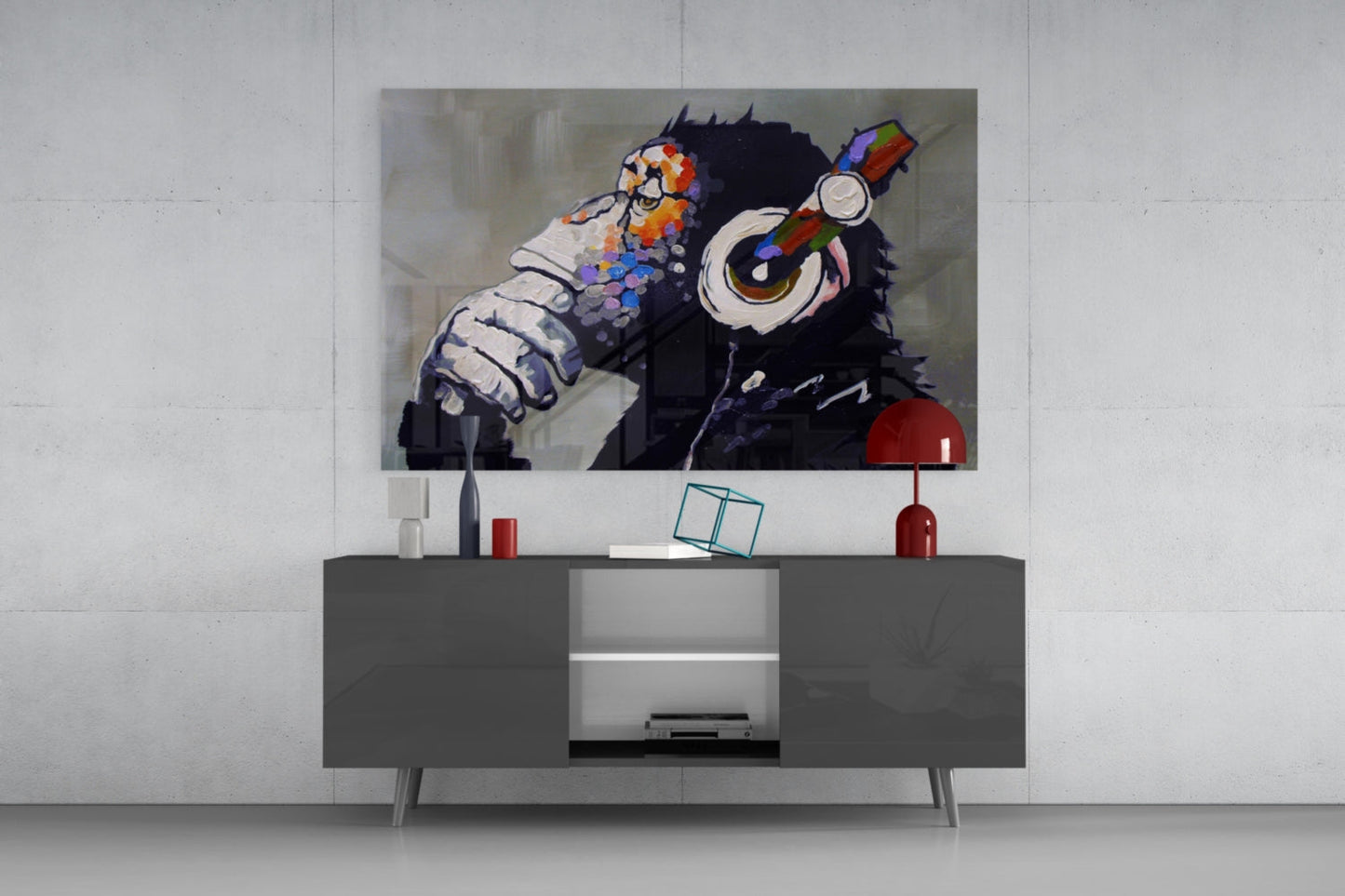 Thinking Monkey glass wall art displaying a black chimp with colorful flowers and headphones mounted above a gray media console in a living room setting.