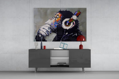 Thinking Monkey glass wall art displaying a black chimp with colorful flowers and headphones mounted above a gray media console in a living room setting.