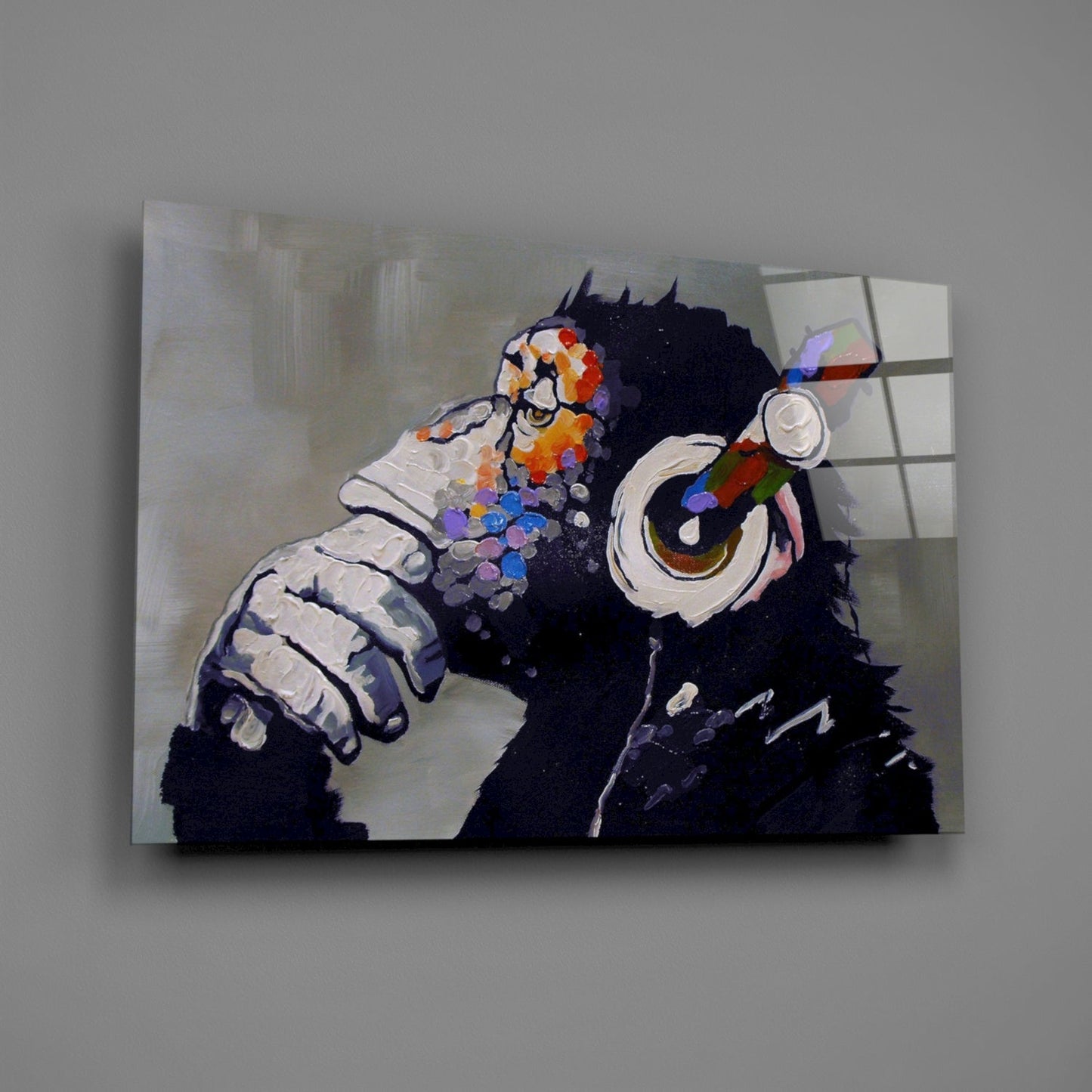 Glass wall art depicting a black chimpanzee wearing colorful headphones with vibrant paint splotches, mounted against a light wall.
