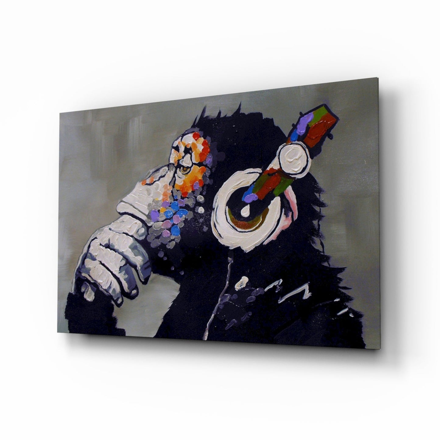 Glass wall art panel displaying a black chimpanzee wearing colorful headphones and holding a paintbrush, shown at an angle against a neutral background.