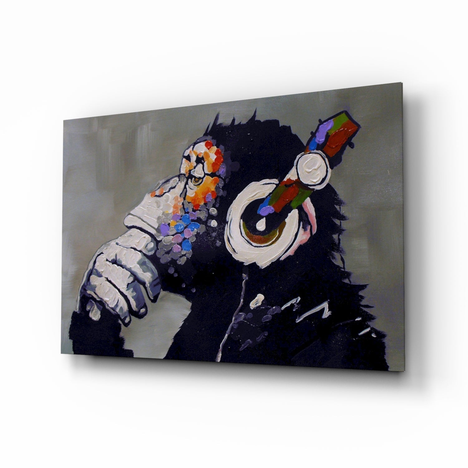 Glass wall art panel displaying a black chimpanzee wearing colorful headphones and holding a paintbrush, shown at an angle against a neutral background.