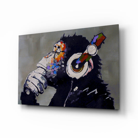 Glass wall art panel displaying a black chimpanzee wearing colorful headphones and holding a paintbrush, shown at an angle against a neutral background.