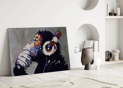 Glass wall art depicting a black silhouette chimpanzee wearing headphones and holding a colorful paintbrush, leaning against a white interior wall.
