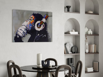 Thinking Monkey glass wall art depicting a black chimp wearing colorful headphones and holding a Rubik's cube, displayed above a round dining table in a modern interior.