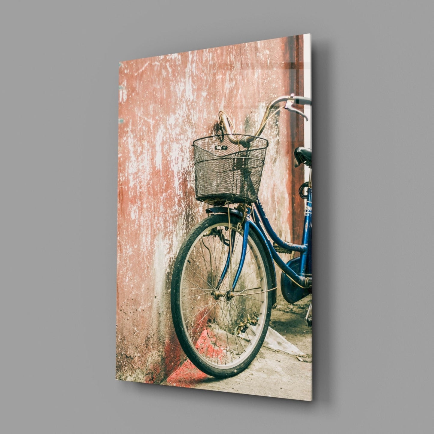 Blue bicycle with mesh basket leaned against weathered terracotta wall, displayed as glass wall art.