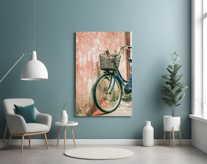 Blue bicycle with wicker basket leaning against weathered terracotta wall, displayed as vertical wall art in modern living room.