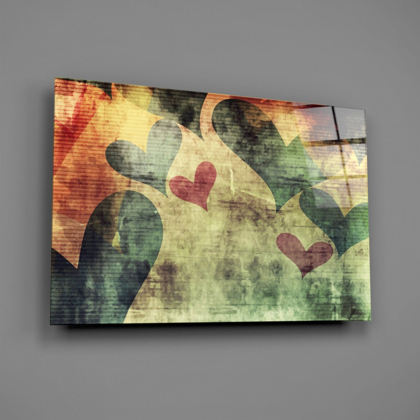 Glass wall art featuring colorful overlapping hearts in red, yellow, green, and orange with distressed texture, displayed at an angle against gray wall.