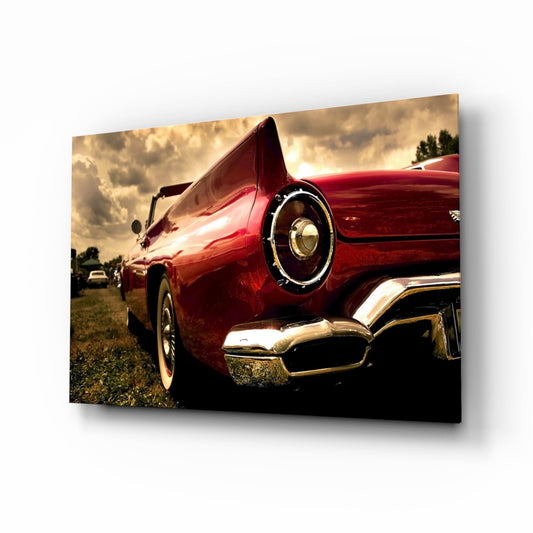 A vibrant red vintage convertible with chrome details and raised tailfin displayed against a dramatic golden-clouded sky at a car show.
