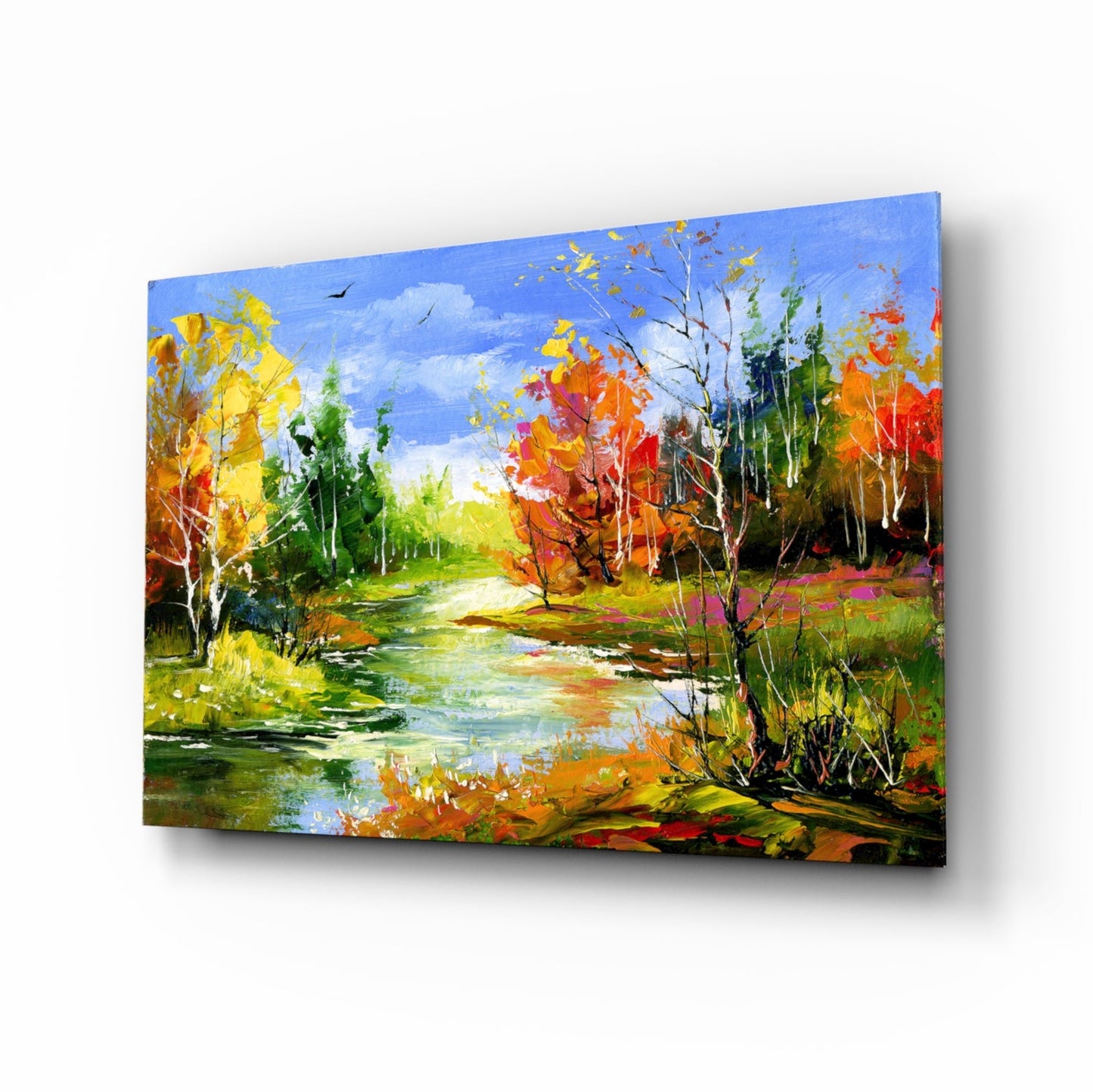 Angled view of a glass wall art panel depicting an autumn landscape with a river, colorful fall trees in yellow, orange, and red, and blue sky.