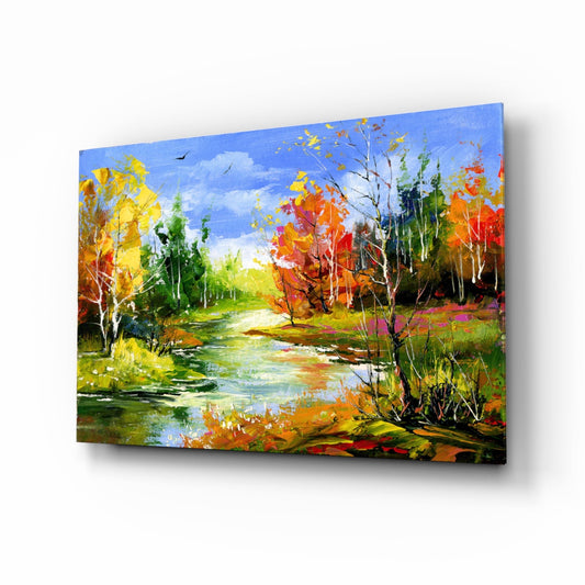 Angled view of a glass wall art panel depicting an autumn landscape with a river, colorful fall trees in yellow, orange, and red, and blue sky.