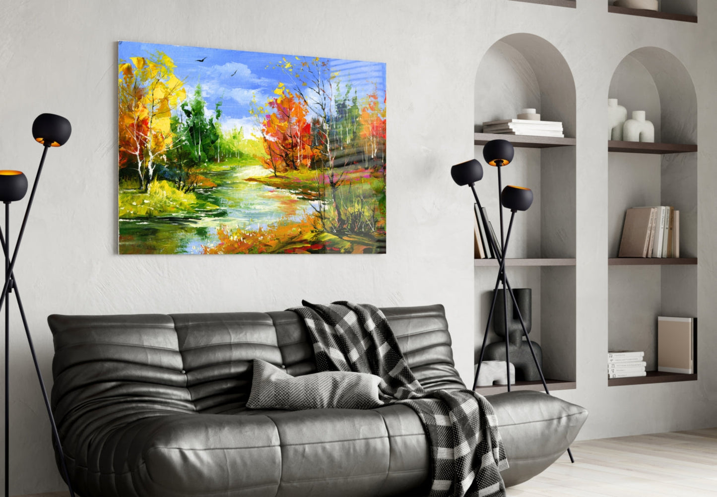 Colorful autumn landscape glass wall art hanging above black leather sofa in modern living room with white shelving.