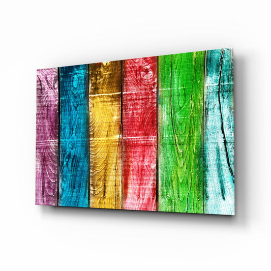 Angled perspective view of colorful glass wall art with six vertical panels painted in pink, blue, gold, red, green, and light blue wood grain patterns.