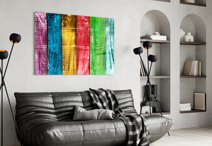 Colorful wood-grain glass wall art with six vertical panels in pink, blue, yellow, red, green, and cyan displayed above a black leather sofa.