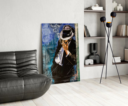 Modern living room with glass wall art depicting a man in black suit and fedora hat against blue textured background, displayed next to gray leather chair and black floor lamp.
