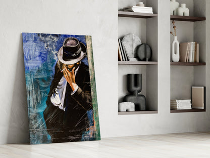 Glass wall art leaning against white wall shows man in black suit and fedora hat against blue textured background.