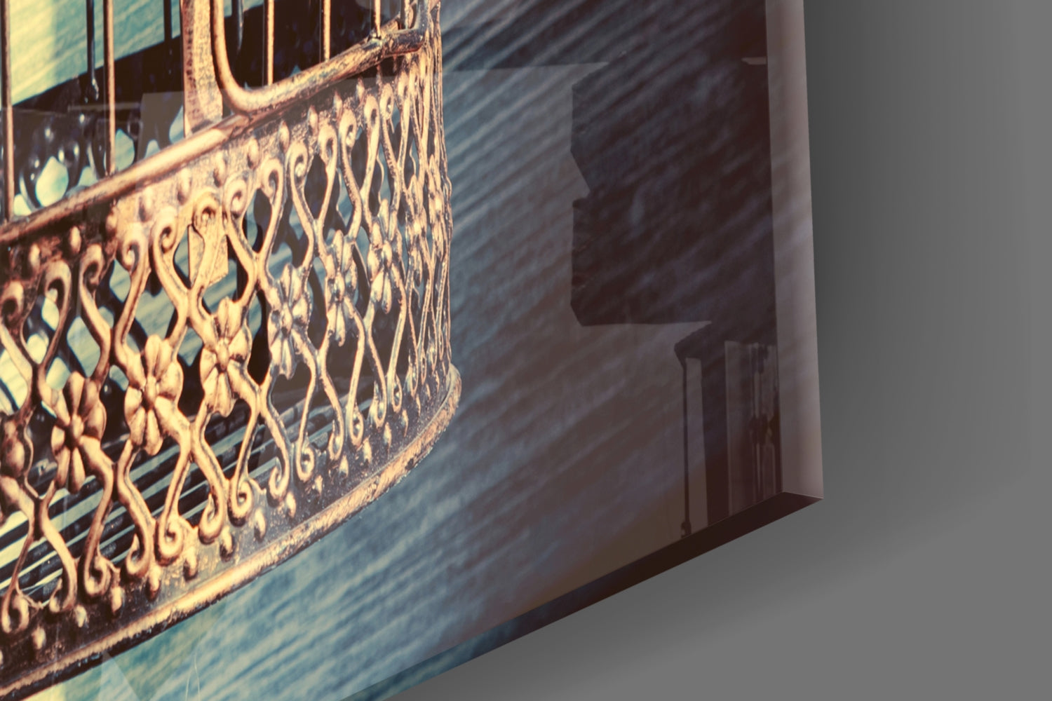 Close-up angled view of decorative gold filigree pattern on blue-toned glass panel with shadow cast on white wall.