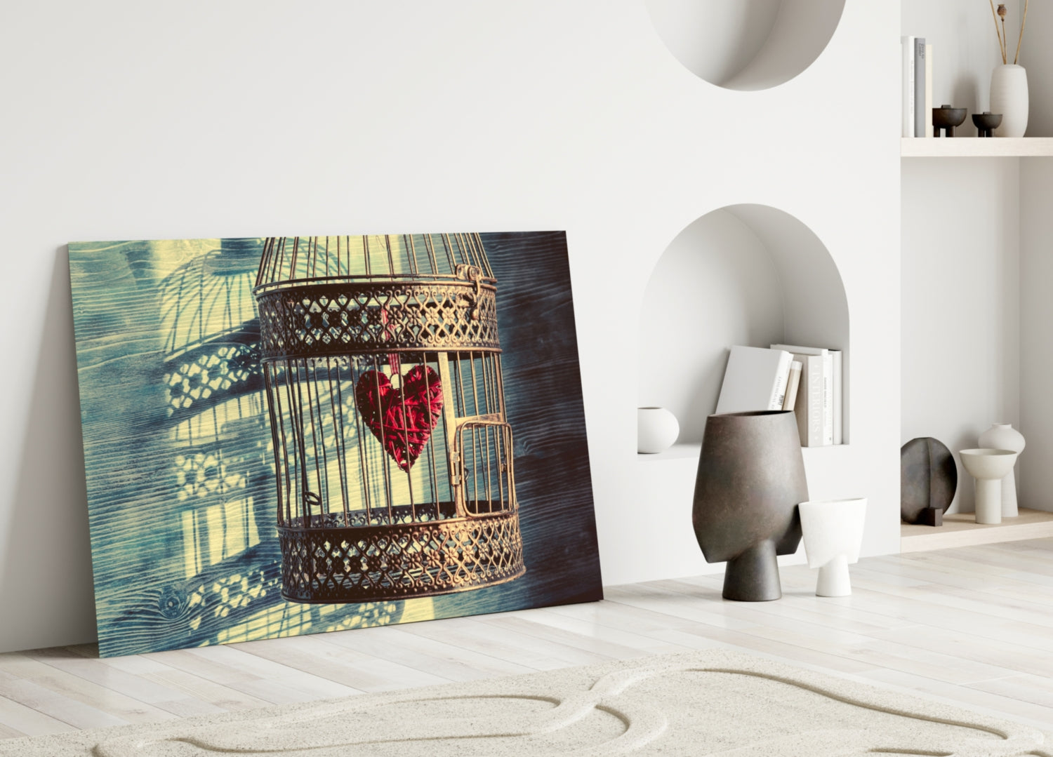 Caged Heart glass wall art leaning against white wall, displaying ornate birdcage with red heart, surrounded by minimalist home decor.
