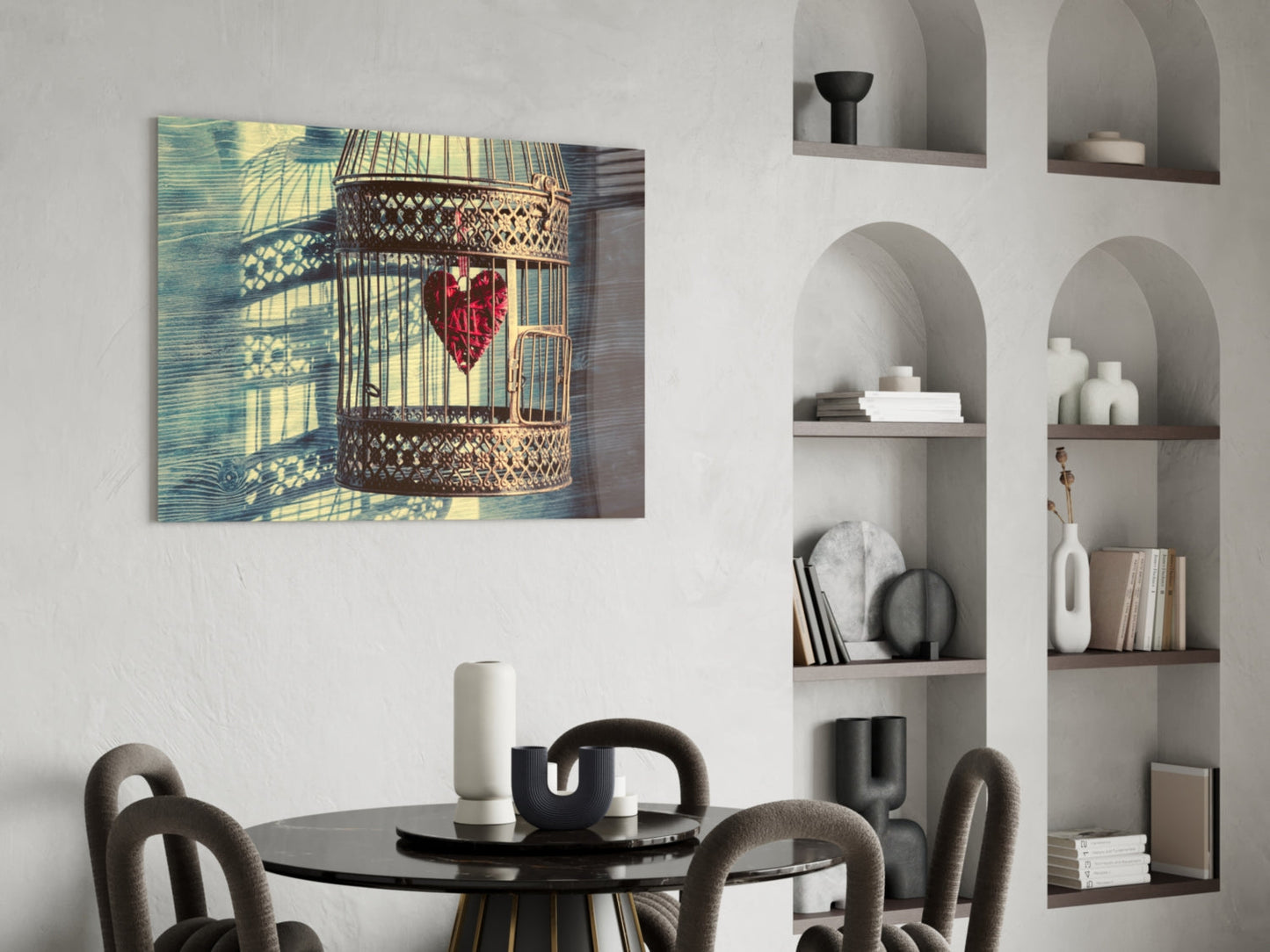 Caged Heart Glass Wall Art displayed above a black round dining table with gray upholstered chairs, showing ornate birdcage with red heart and blue-yellow background.