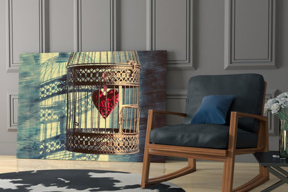 Glass wall art depicting ornate birdcage with red heart inside, displayed in modern room setting beside wooden chair.