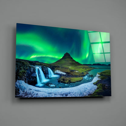 Angled view of glass wall art displaying an Icelandic landscape with aurora borealis, waterfall, and mountain under night sky.