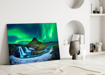 Northern Lights glass wall art leaning against white wall displays green aurora borealis, waterfall, and mountain landscape.