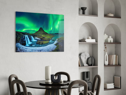 Northern Lights glass wall art displaying vibrant green aurora borealis over Icelandic waterfall and mountain landscape, hung above modern dining table.