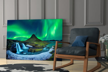 Northern Lights glass wall art displayed in modern living room beside wooden chair, showing green aurora borealis over Icelandic landscape with waterfall.