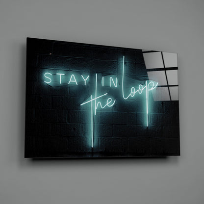 Cyan neon "Stay in the Loop" text glows against dark brick wall on angled glass panel displaying mounting hardware.