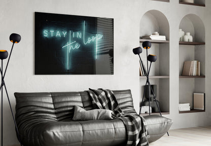 Neon "Stay in the Loop" glass wall art glowing cyan above black leather sofa in modern living room with white shelving.