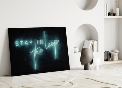 Neon glass wall art with turquoise "Stay in the Loop" text displayed on light wood floor in minimalist room setting.