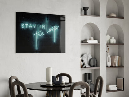Neon "Stay in the Loop" glass art displayed on white brick wall above black round table with curved chairs and styled shelving.