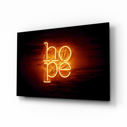 Neon glass wall art displaying "hope" in glowing gold letters against a dark wooden background, mounted on a wall at an angle.