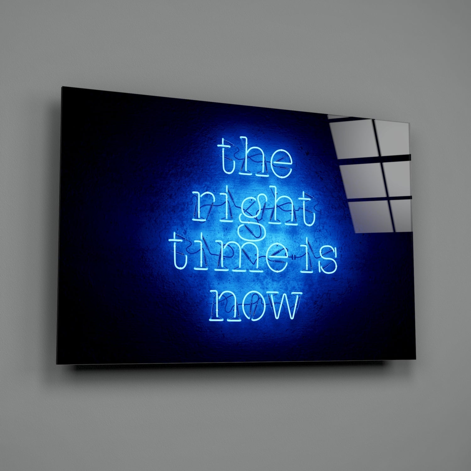 Blue neon sign reading "the right time is now" mounted on dark glass panel against gray wall.