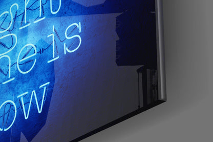 Blue neon glass wall art with cyan lettering spelling "The Right Time Is Now," angled perspective view against white wall.