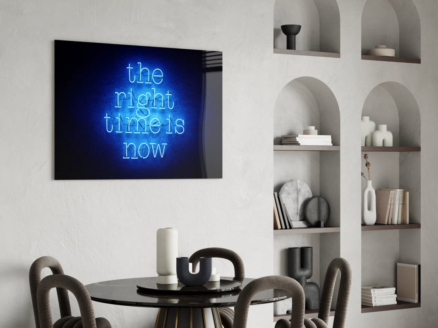 Blue neon "the right time is now" glass art displayed on white wall above black dining table with gray chairs and white shelving unit.