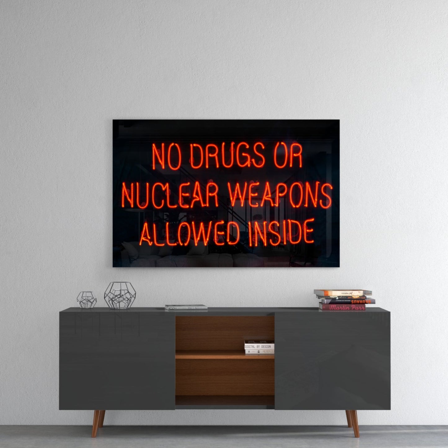 Red neon sign reading "NO DRUGS OR NUCLEAR WEAPONS ALLOWED INSIDE" mounted above gray mid-century modern console table against white wall.