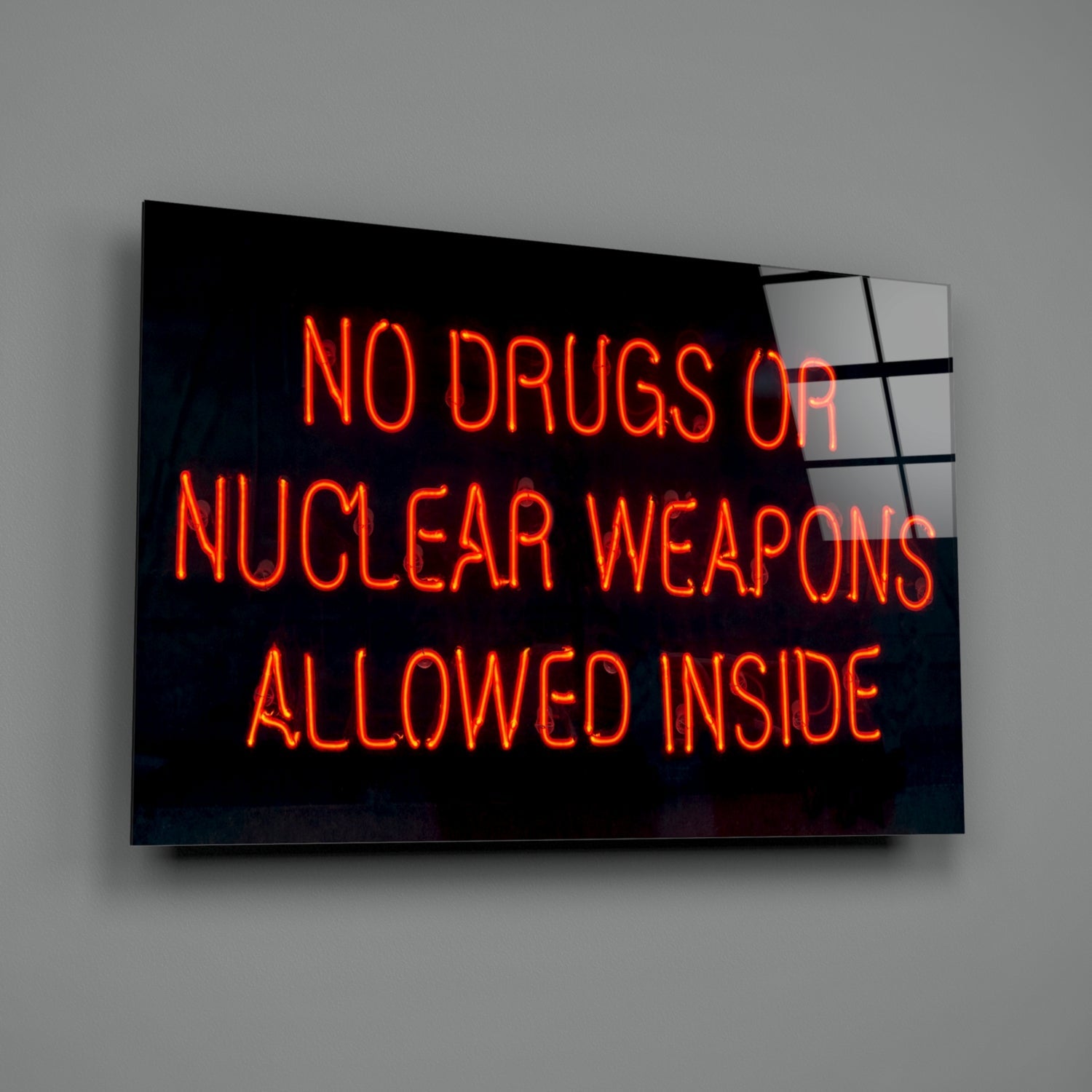 Neon sign on black glass displaying red glowing text reading "NO DRUGS OR NUCLEAR WEAPONS ALLOWED INSIDE" mounted on gray wall.