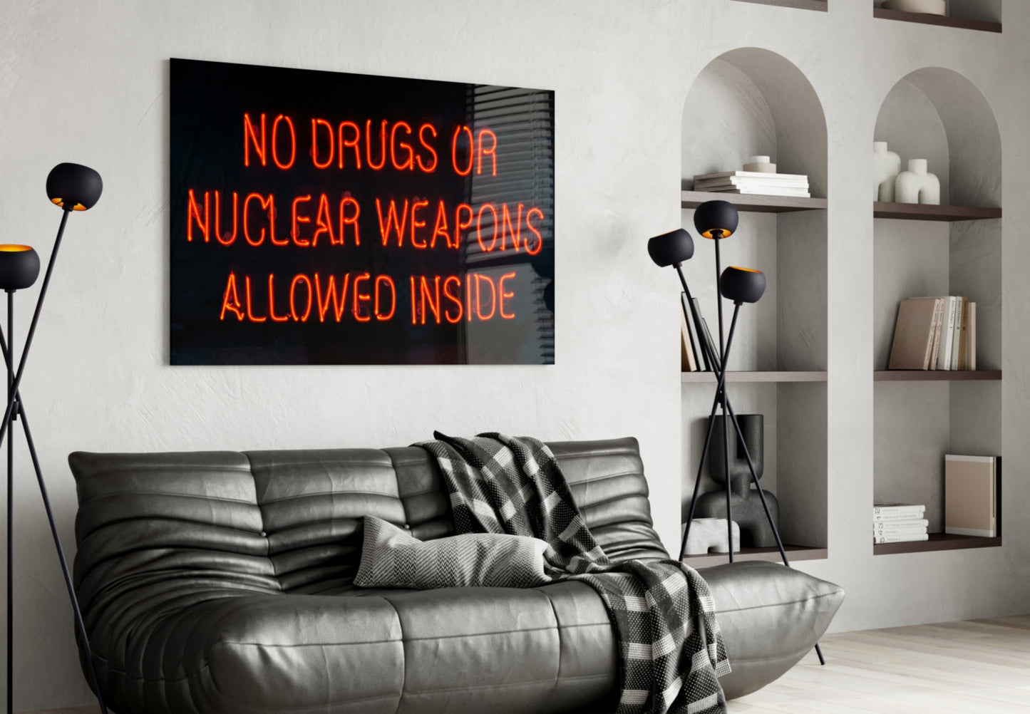 Red neon sign reading "NO DRUGS OR NUCLEAR WEAPONS ALLOWED INSIDE" displayed above gray leather sofa in modern living room with white built-in shelving.