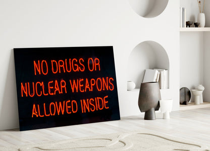 Neon glass wall art with red lettering reading "NO DRUGS OR NUCLEAR WEAPONS ALLOWED INSIDE" displayed in minimalist white interior.
