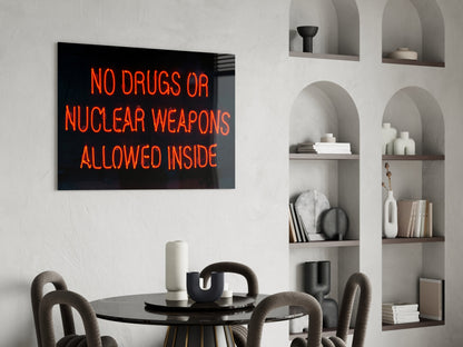 Neon glass wall art displaying "NO DRUGS OR NUCLEAR WEAPONS ALLOWED INSIDE" in orange text above a dining table.