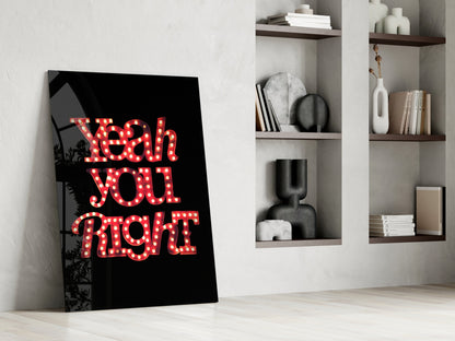 Black glass wall art with red marquee-style lettering reading "Yeah you right" leaning against white wall beside wooden shelving unit.