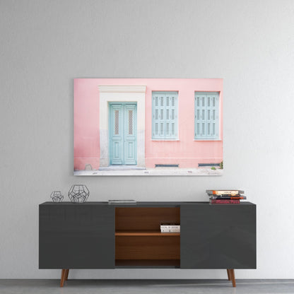 Pink house glass wall art hung above dark mid-century credenza, displaying pastel pink facade with blue shuttered door.