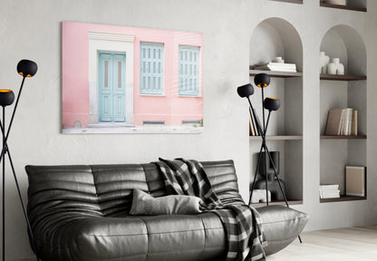 Pink House Glass Wall Art displaying turquoise doors and shutters, hung above black leather sofa in modern living room.