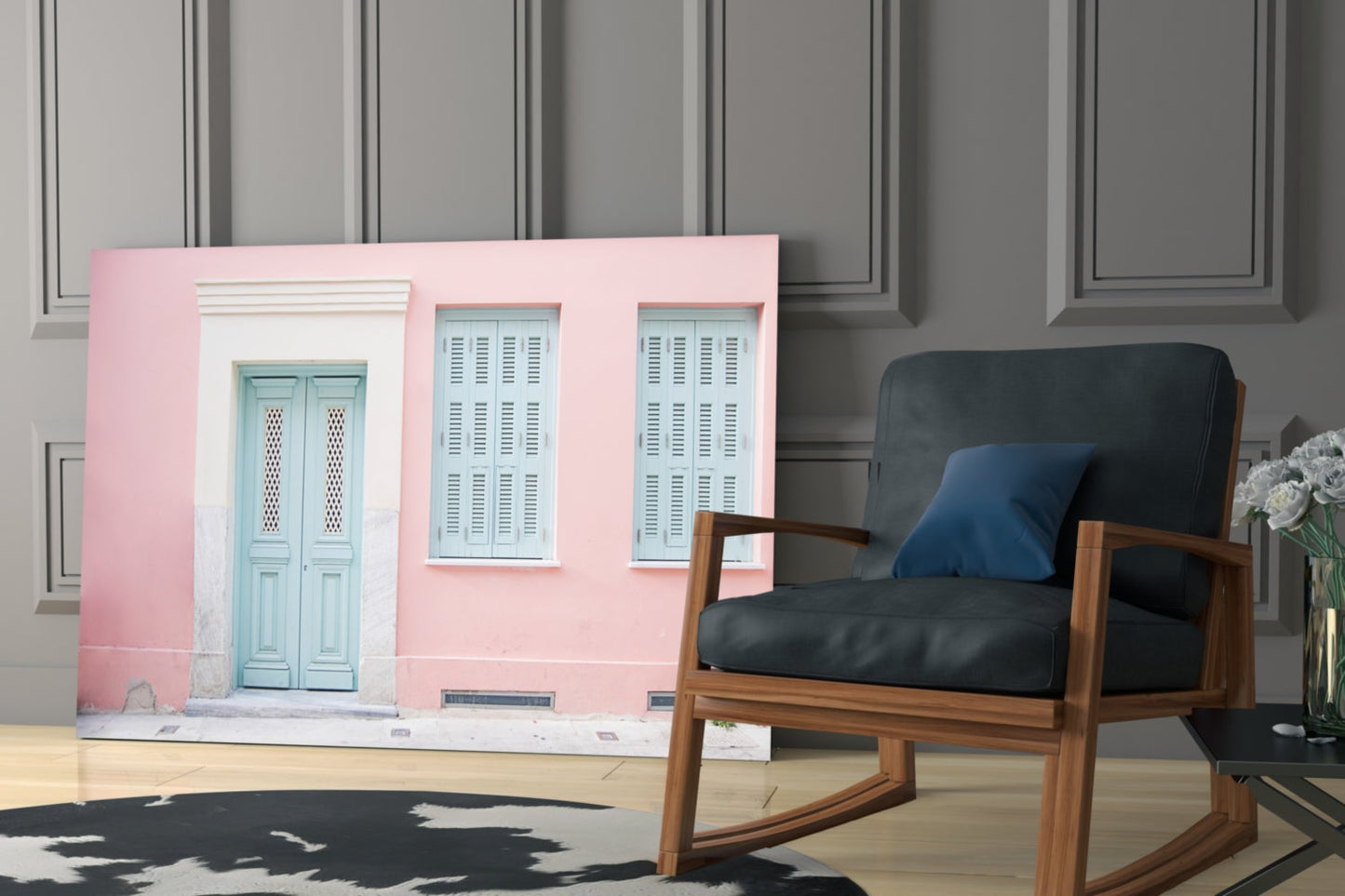 Pink house glass wall art displayed behind mid-century wooden chair with black cushions in modern interior setting.